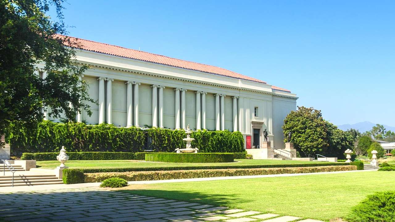 A white building with columns surrounded by a garden with green grass and sculptures