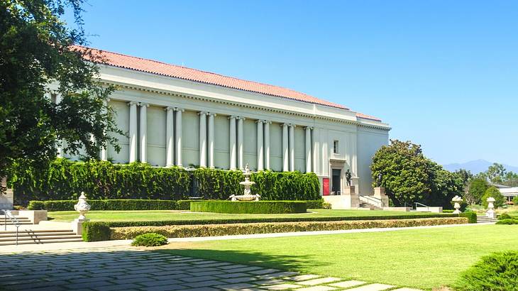 A white building with columns surrounded by a garden with green grass and sculptures