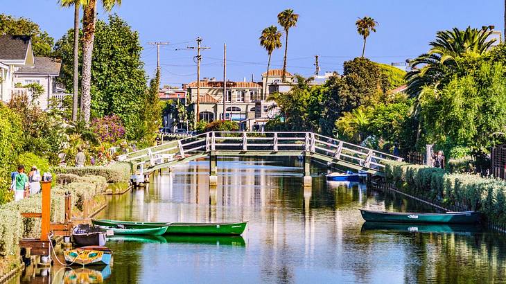 A canal with trees on either side, a small bridge across it, and kayaks on the water