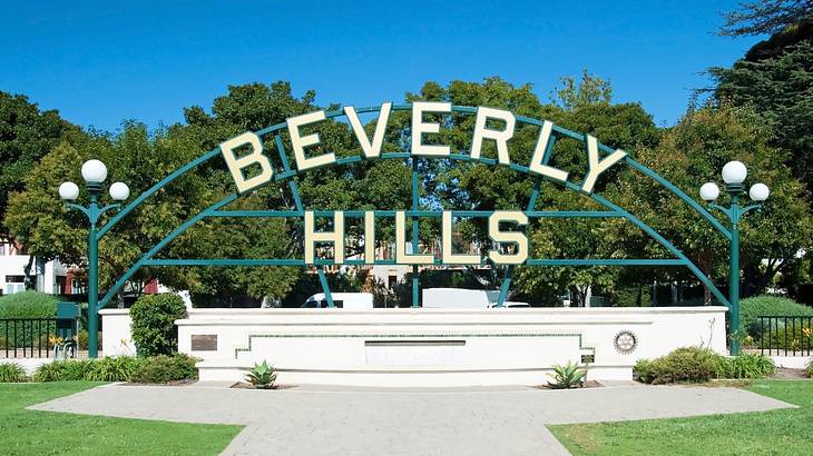 A sign that says "Beverly Hills" with a lawn, trees, and a path around it