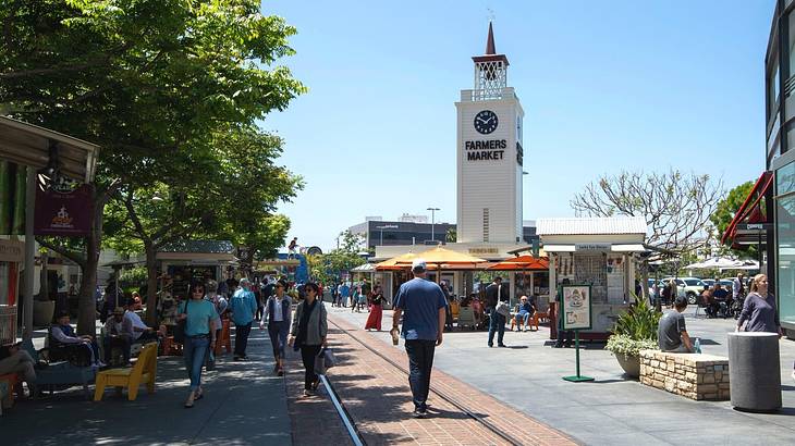 A pedestrian street and a white clock tower that says "Farmers Market"