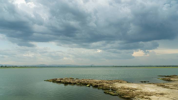 Flat rocky surface surrounded by dark water and clouds above