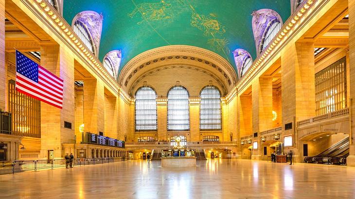 A train station terminal with big windows, a green roof, and a US flag