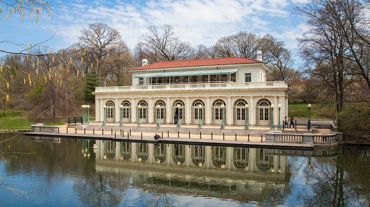 An old-fashioned boathouse next to a lake and bare winter trees