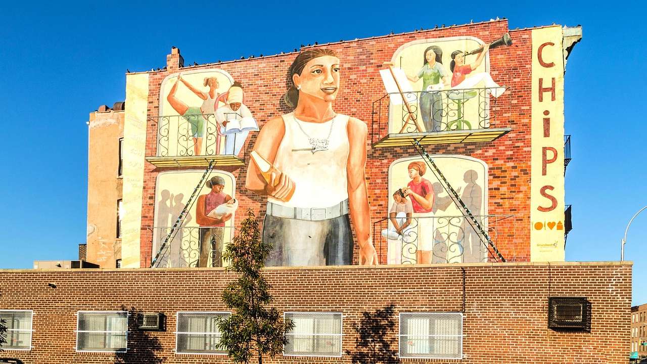 A building with a street art mural on it, featuring women in their apartments