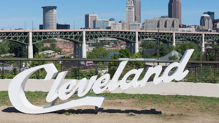 A white sign that says "Cleveland" on the grass next to a city skyline