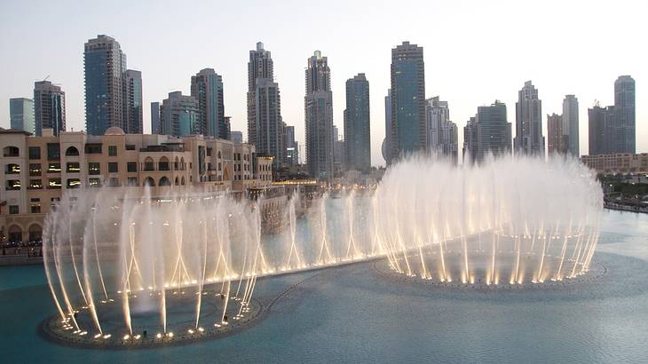 Lit up water fountains dancing in the middle of city buildings at sunset
