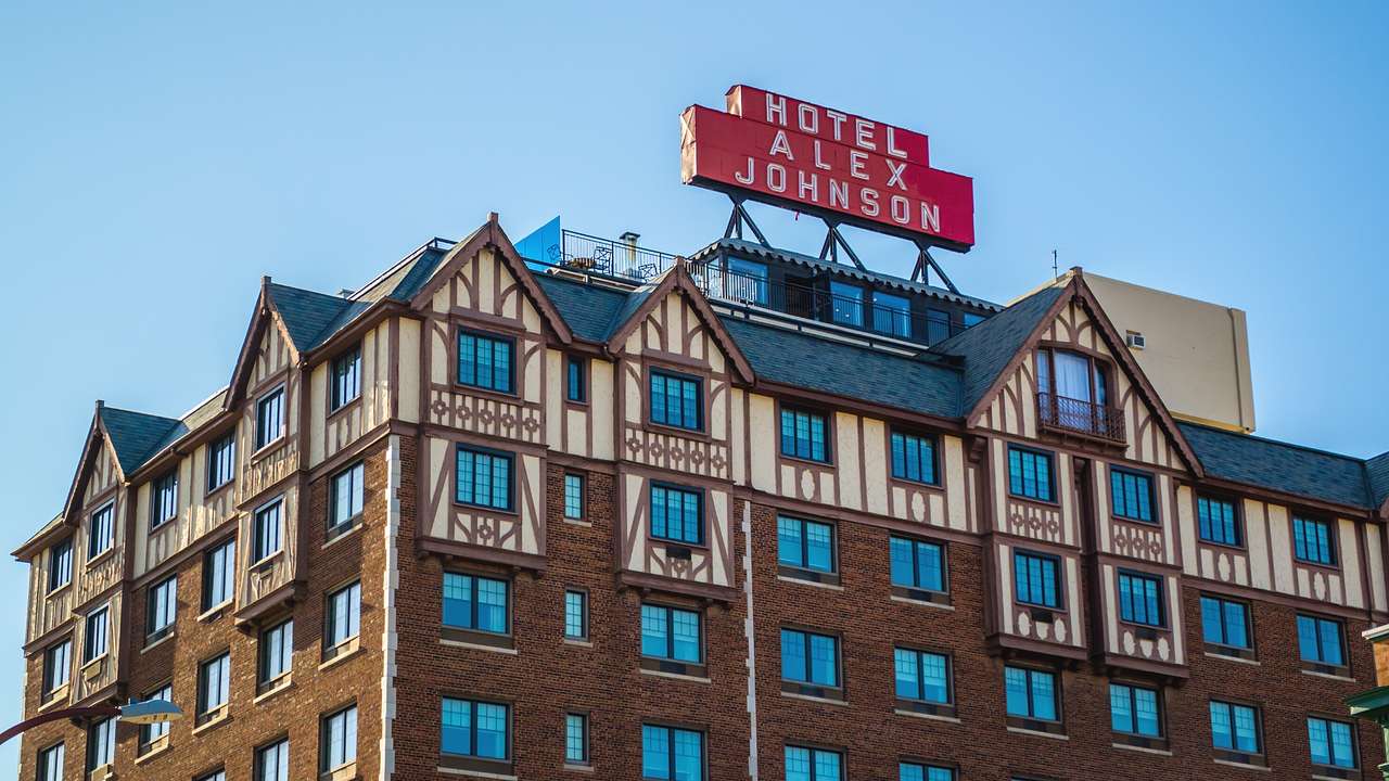 A large hotel with brick and Tudor details and a red "Hotel Alex Johnson" sign