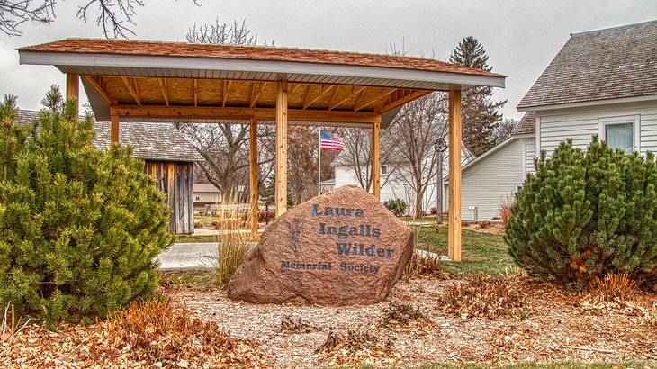 A rock that says "Laura Ingalls Wilder Memorial Society" next to a house and garden