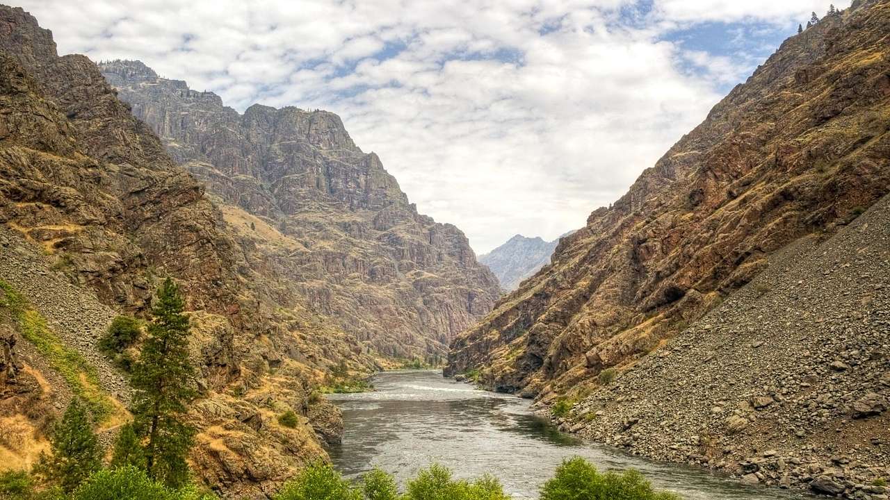 A river winding through a rugged brown canyon under a partly cloudy sky