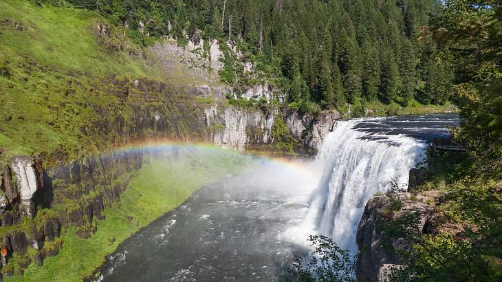A waterfall surrounded by green cliffs with trees, with a rainbow over the water