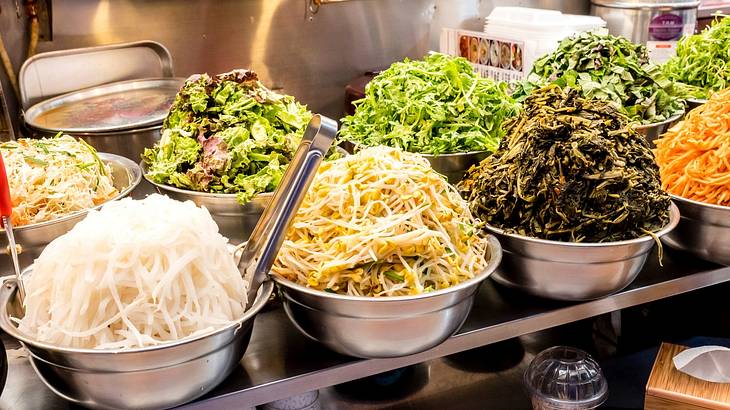 Big silver bowls piled high with fermented foods on a table from above