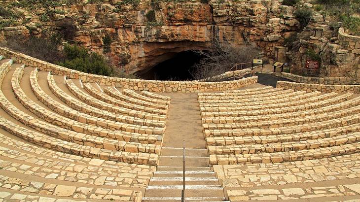 A semi-circle of wide steps made of rocks, leading downwards to a cave