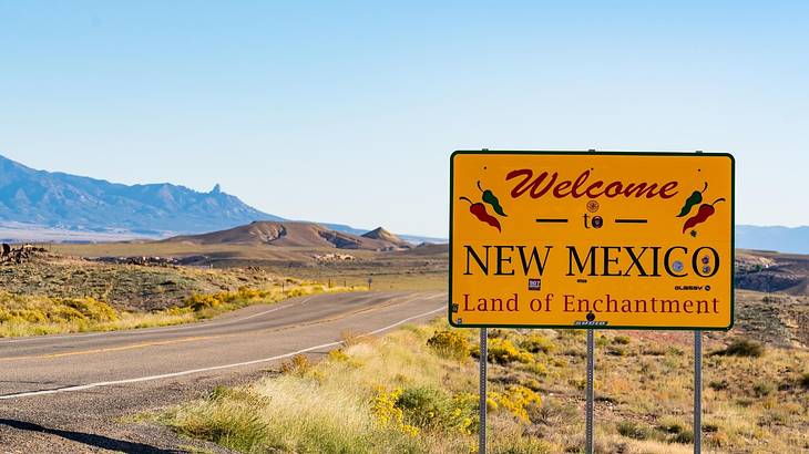 A yellow sign with "Welcome to New Mexico, Land of Enchantment" along a grassy road
