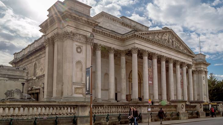 A large stone structure with columns next to a street under a blue sky with clouds