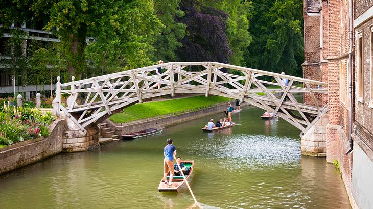 Boats on a river passing under a wooden bridge connecting a building to a wooded area