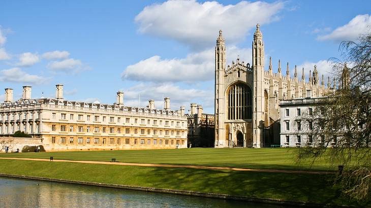 A Gothic chapel surrounded by buildings with a huge lawn in front and a river