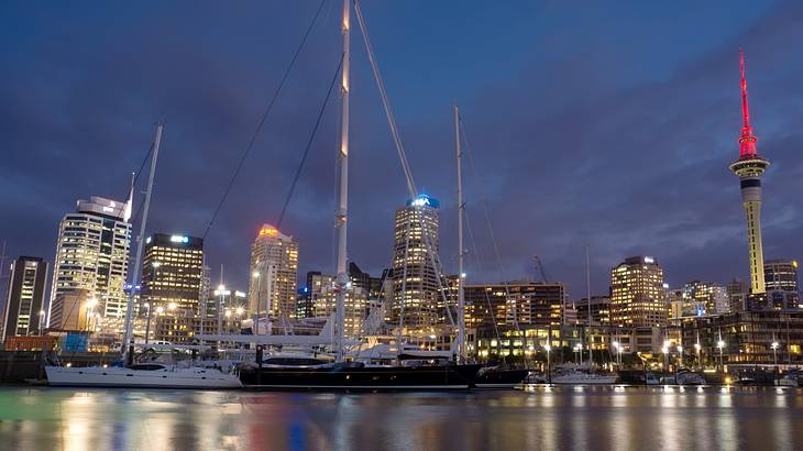 Lit up tall city buildings with big boats on water in front at night Lit up tall city buildings with big boats on water in front at night
