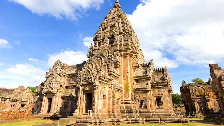 An old Khmer temple made of bricks with ancient carvings and green grass in front