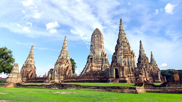 Wide angle view of temple ruins with green lawns and trees around and blue sky above