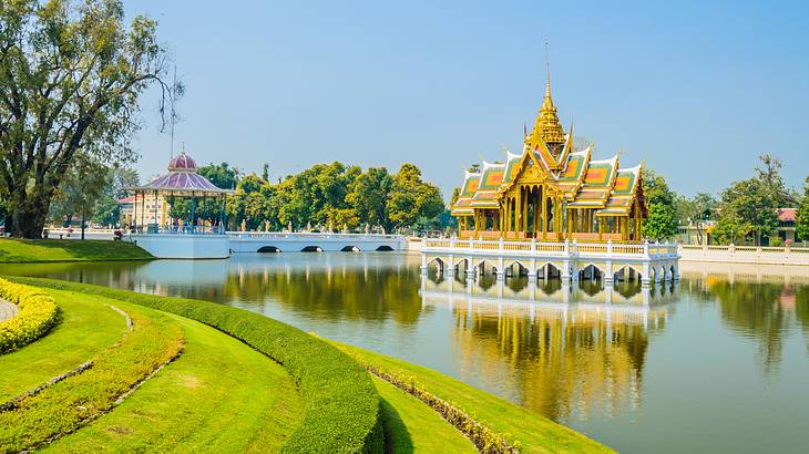 A gold-colored palace in the middle of a pond with green lawns and trees surrounding