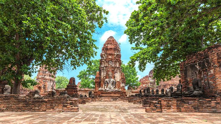 A sitting sandstone Buddha monument surrounded by temple ruins and trees