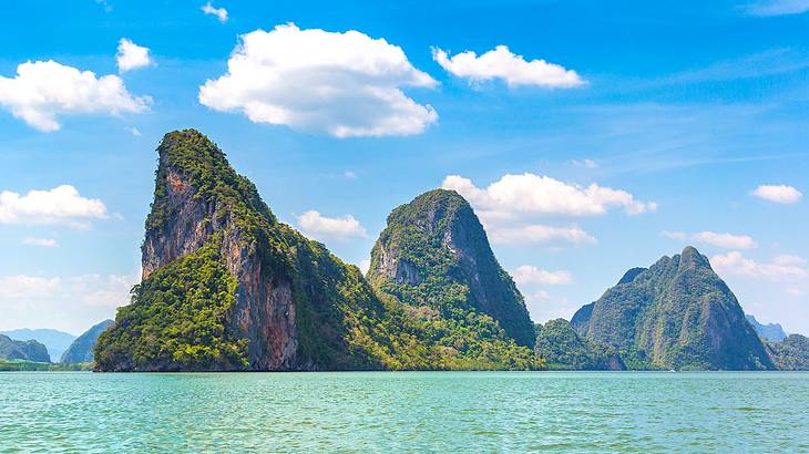 Large green limestone cliffs surrounded by turquoise water on a partly cloudy day