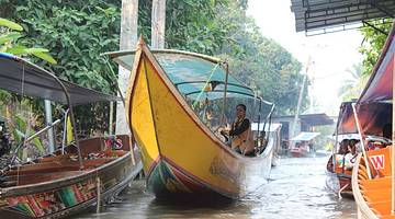 A yellow long tail boat with a person on it moving through a Khlong canal in Bangkok