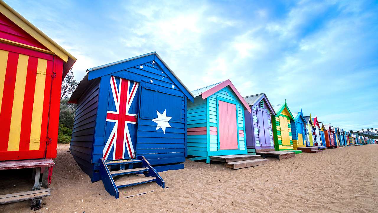 Colourful and bright wooden beach huts lining a sandy beach on a nice day