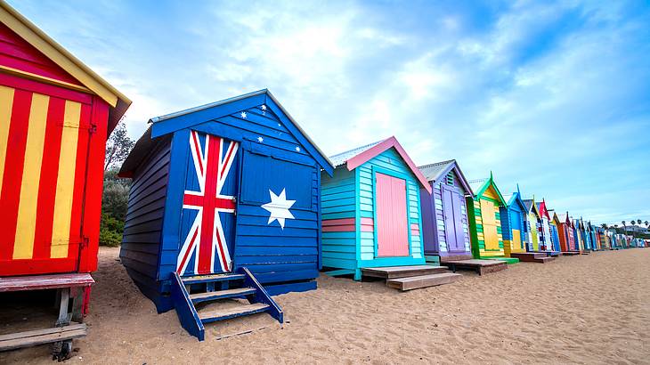 Colourful and bright wooden beach huts lining a sandy beach on a nice day