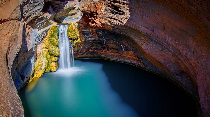 A waterfall flowing into a turquoise pool below in between rocks