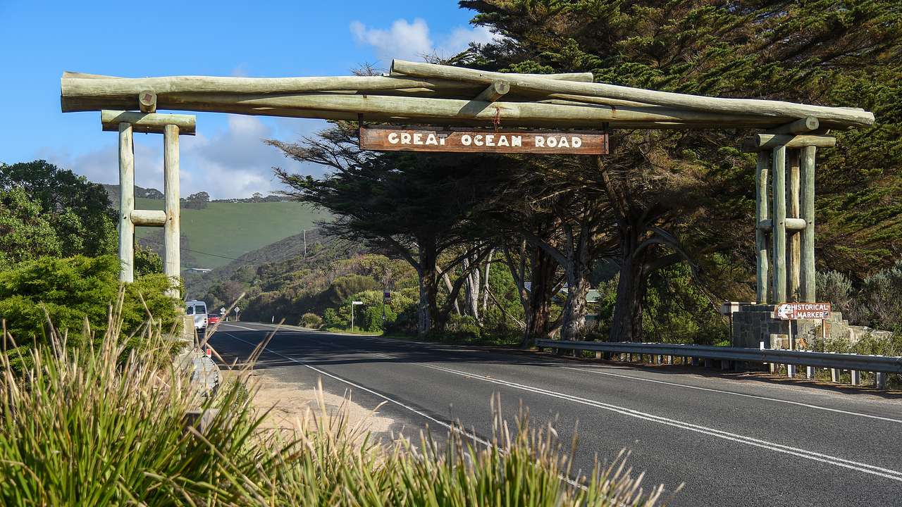 A sign "Great Ocean Raod" over a road next to trees and shrubs on a nice day