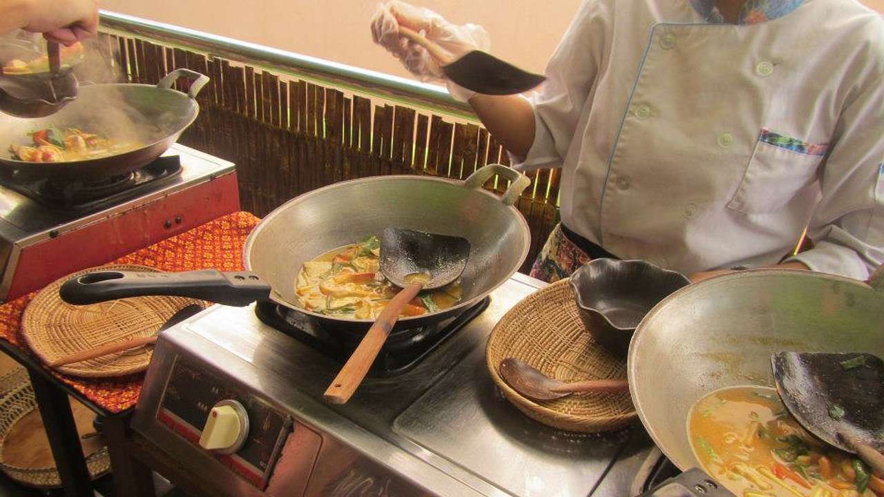 People cooking vegetables in several woks on a stove from above