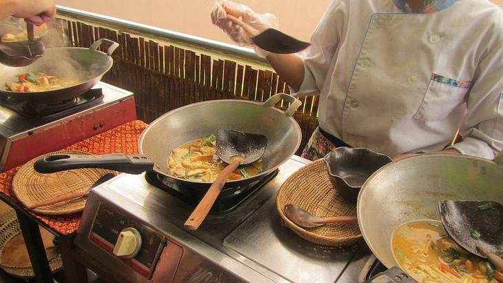 People cooking vegetables in several woks on a stove from above