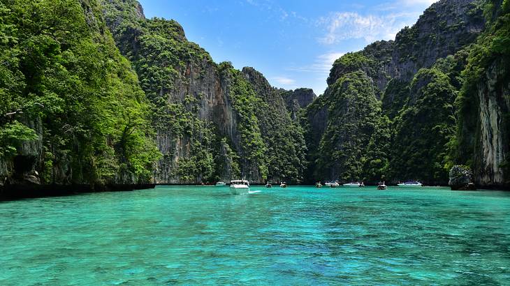 Tourist boats floating and moving on turquoise water surrounded by limestone cliffs