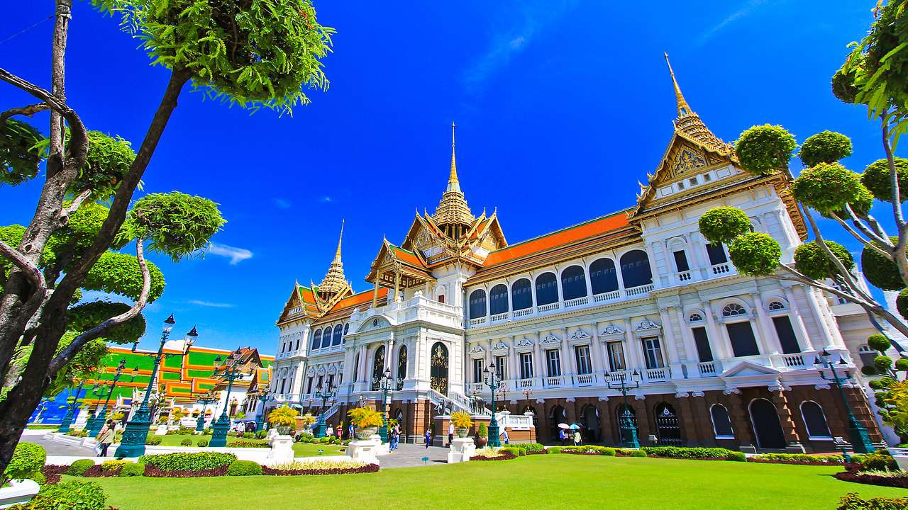 A large white palace building with a gold roof facing a manicured lawn and bushes