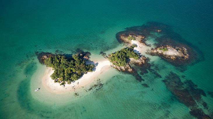 A small island with a sandy beach surrounded by emerald water from above