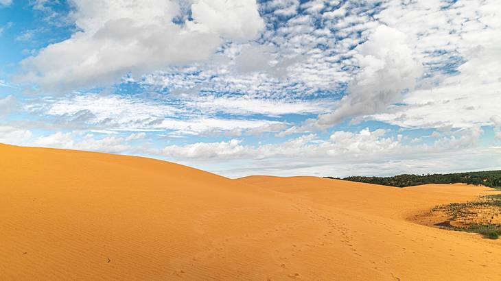 Orange colored sand dunes under a partly cloudy sky