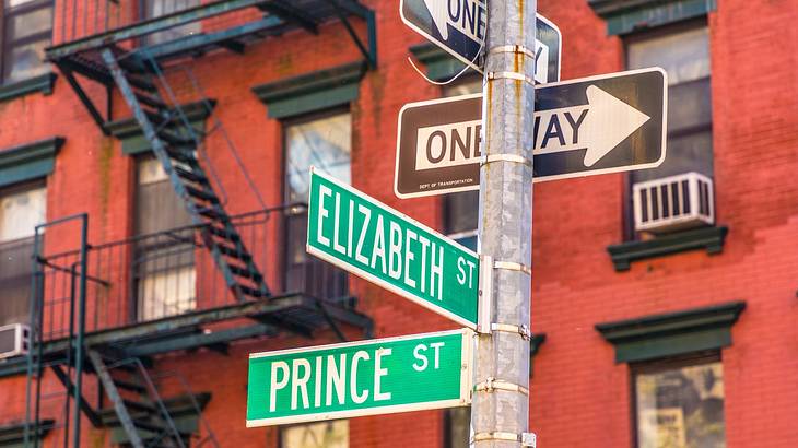 Several named street signs on a post in front of a red brick building