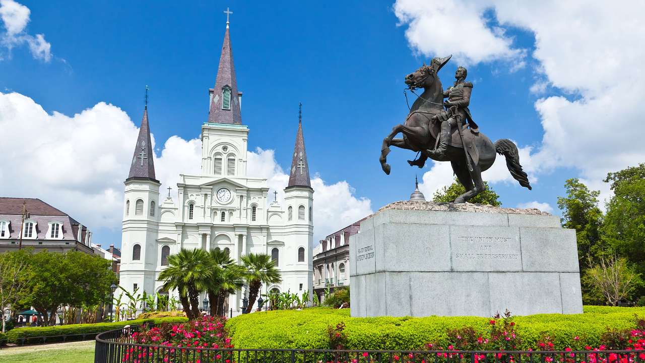 A white castle-style building next to greenery, flowers, and a pedestal statue