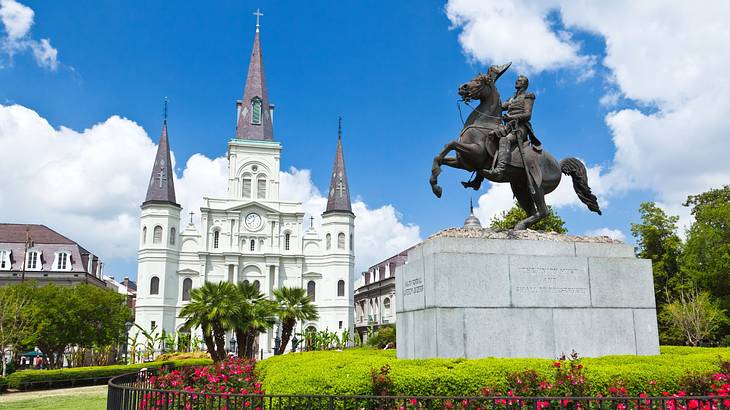 A white castle-style building next to greenery, flowers, and a pedestal statue
