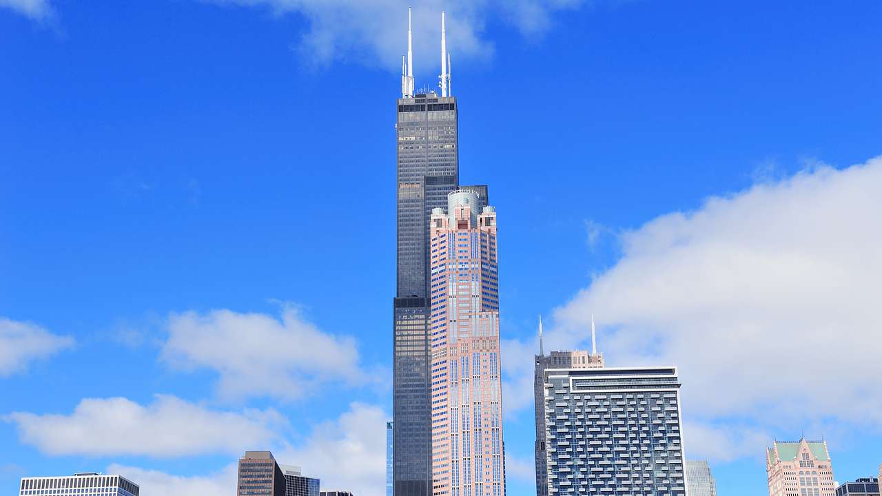 Two tall skyscrapers with smaller buildings around them and a partly cloudy sky
