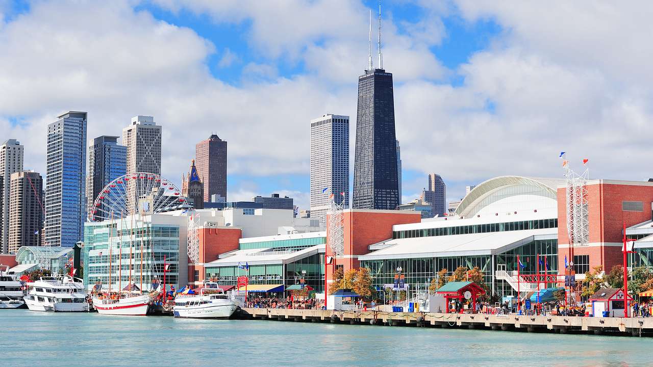 A long pier filled with docked boats, people walking, buildings, and shops