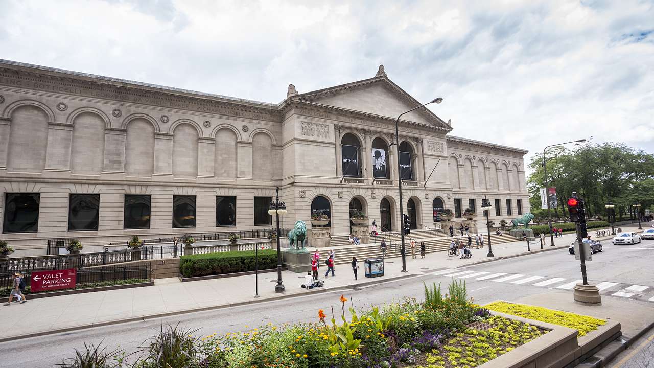 A large stone building viewed from across the street with people on the sidewalk