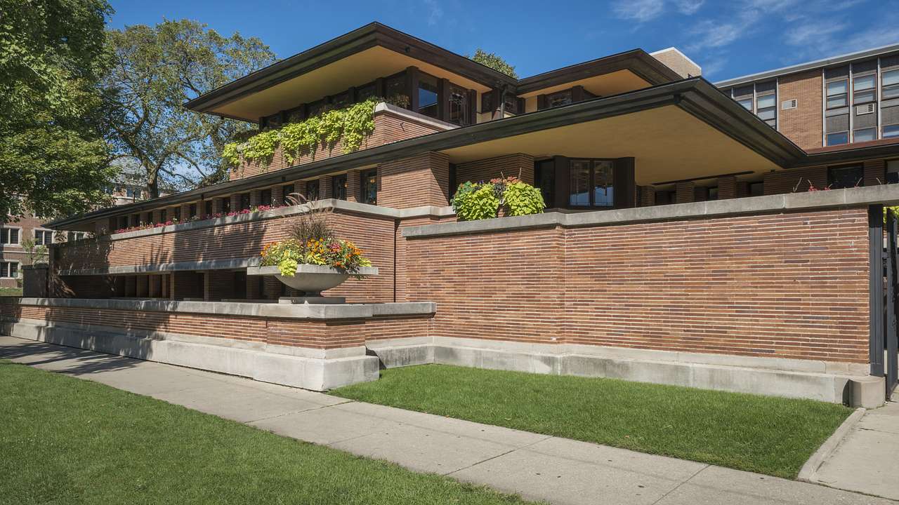 A large brick multi-level house with decorative plants, a lawn, and a sidewalk