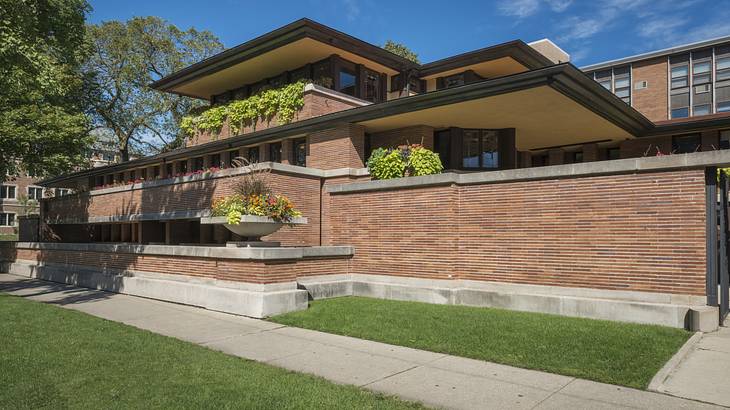 A large brick multi-level house with decorative plants, a lawn, and a sidewalk