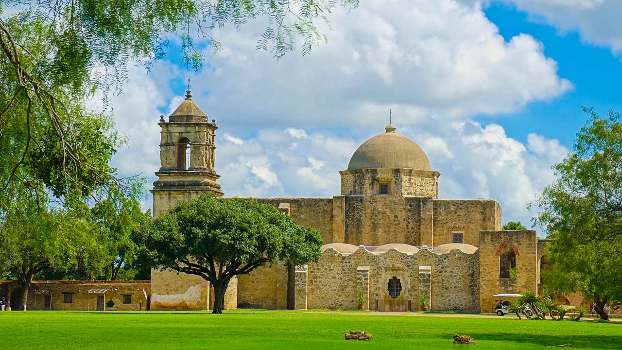 A domed church with a bell tower next to the grass under a blue sky with white clouds