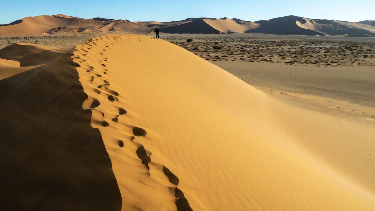 Salt and clay ground surrounded by high sandy dunes with footprints