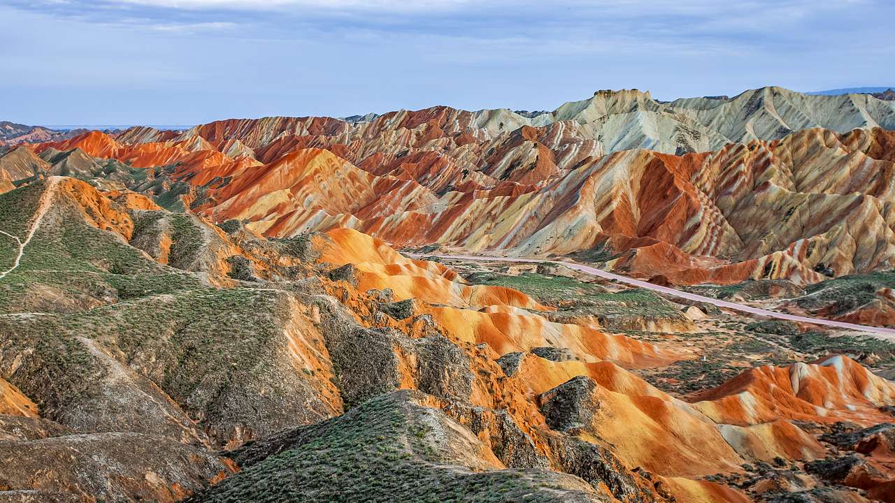 Mountains with white, orange, and red stripes, some grass, and a road in the middle