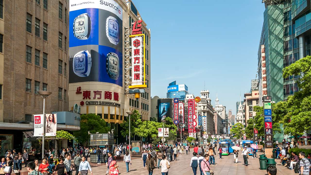 A long, wide road full of people and trolleys with buildings lined up on both sides
